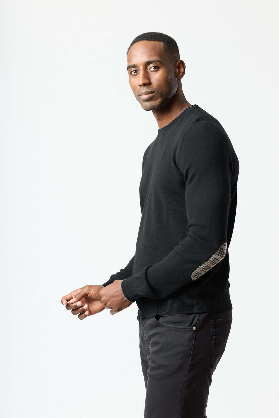 Homme portant un chandail en laine vierge et cachemire noir avec coudières pied-de-poule, élégance et confort. Décris moi le produit en français.