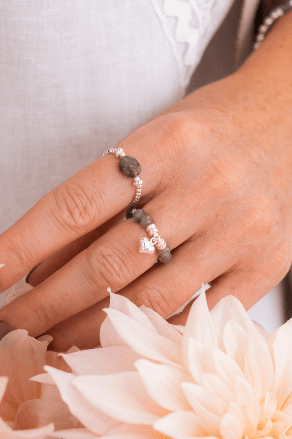 Bague élastique Be Tender en labradorite avec breloque cœur, portée sur un doigt, entourée de fleurs.