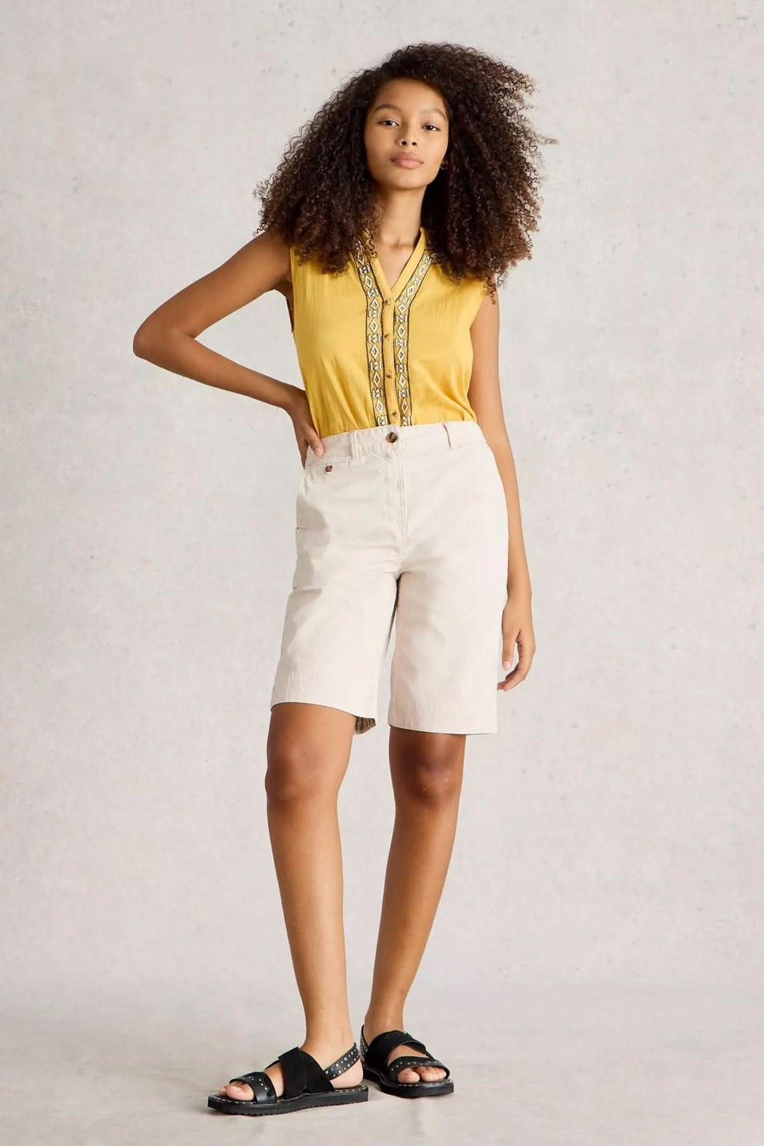 Modèle portant des bermudas en coton naturel, look estival élégant avec haut jaune et sandales.