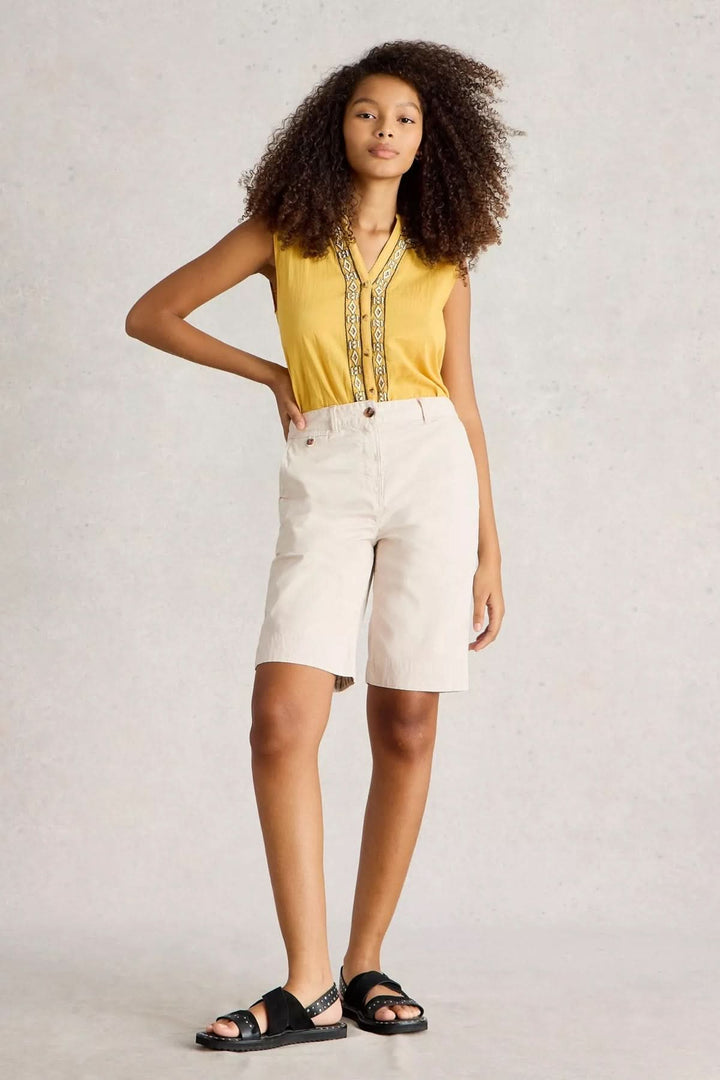 Modèle portant des bermudas en coton naturel, look estival élégant avec haut jaune et sandales.