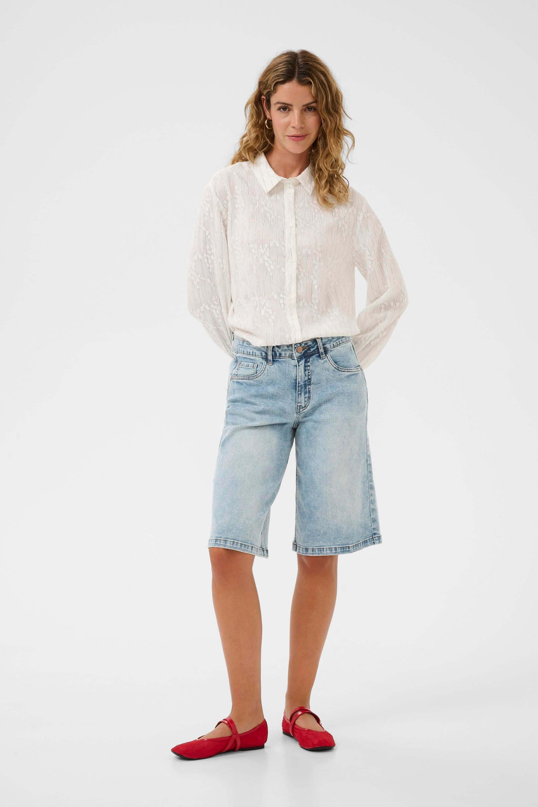 Femme portant le Bermuda Joani en denim, coupe droite, longueur genou, style décontracté et soigné, avec chemise et chaussures rouges.