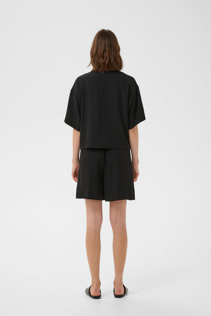 Femme portant un Bermuda Varina fluide taille élastique ceinturé avec coupe droite et poches latérales, vu de dos en studio.