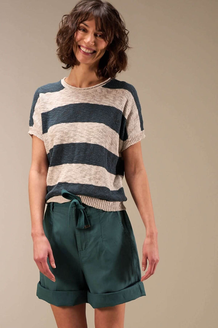 Femme souriante portant un pull à rayures et un bermuda décontracté en été, style bohème et naturel.