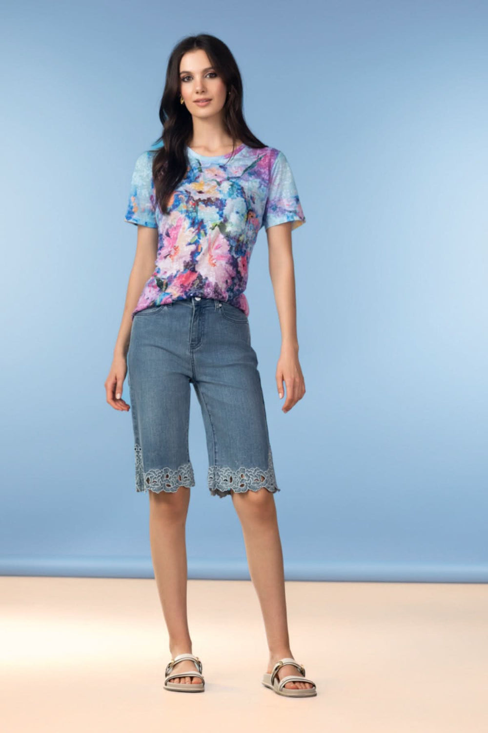 Femme portant un Bermuda en denim à finitions brodées, associé à un haut fleuri, sur fond bleu.
