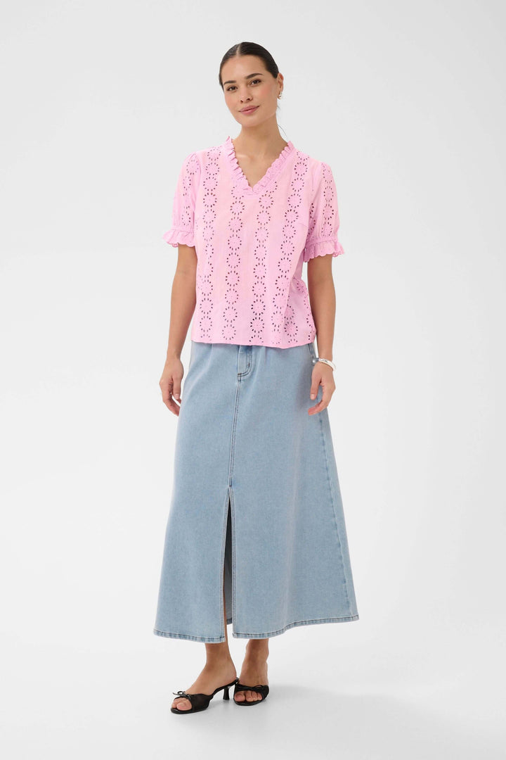 Femme portant la Blouse Dona brodée à manches courtes avec encolure volantée, associée à une jupe longue en jean.
