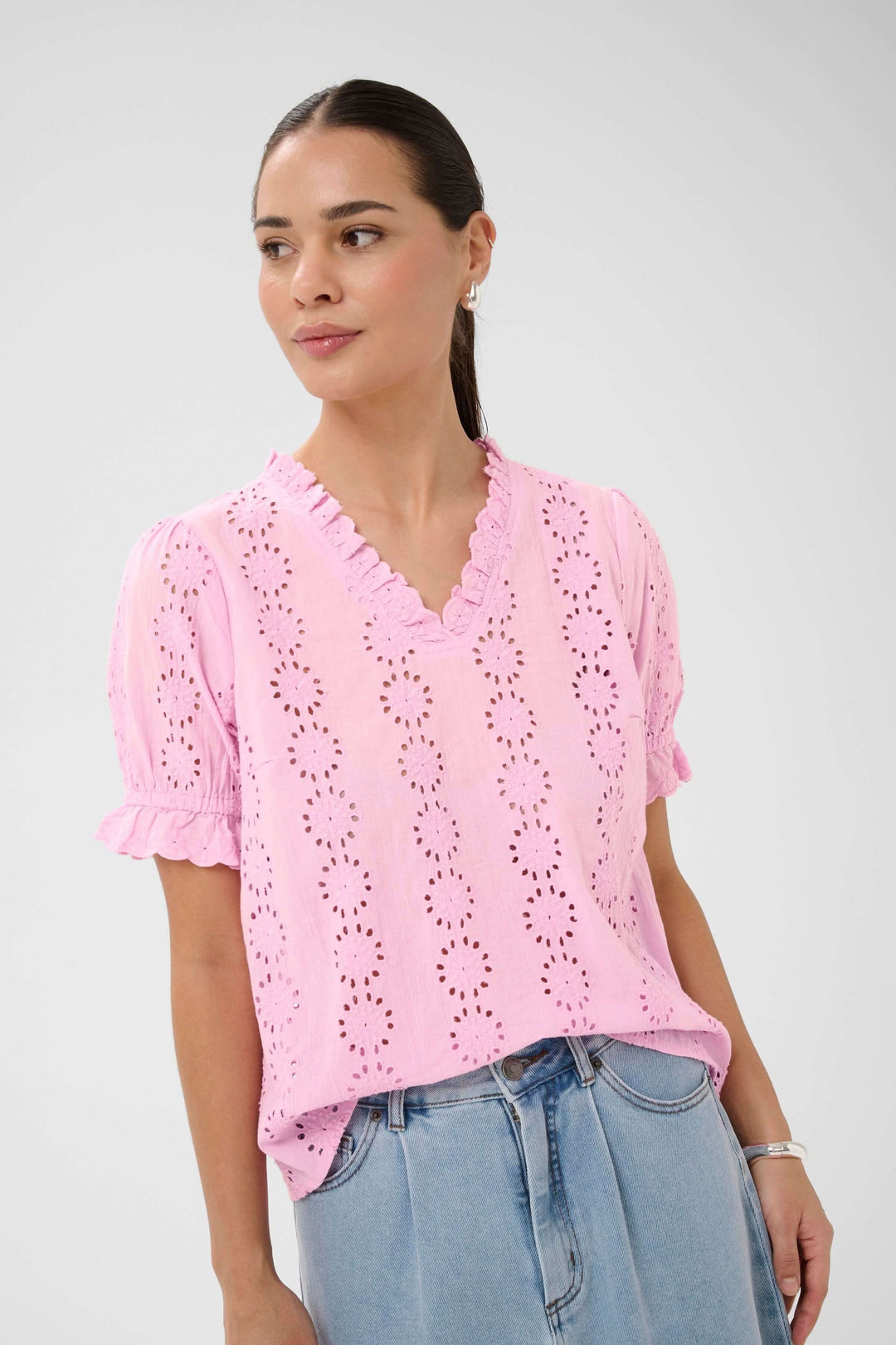 Blouse Dona brodée à manches courtes avec encolure volantée, broderies ajourées, portée avec un jean, look élégant et décontracté.