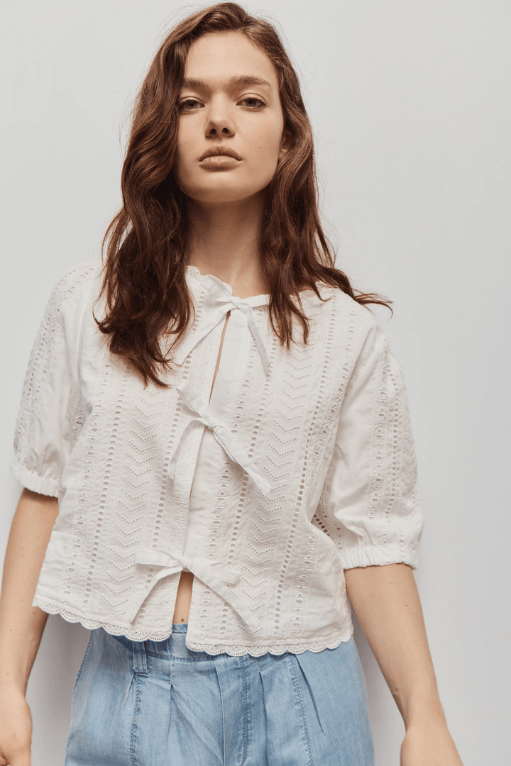 Modèle portant la Blouse Giana brodée à nouer avec broderies ajourées et manches courtes, idéale pour l&