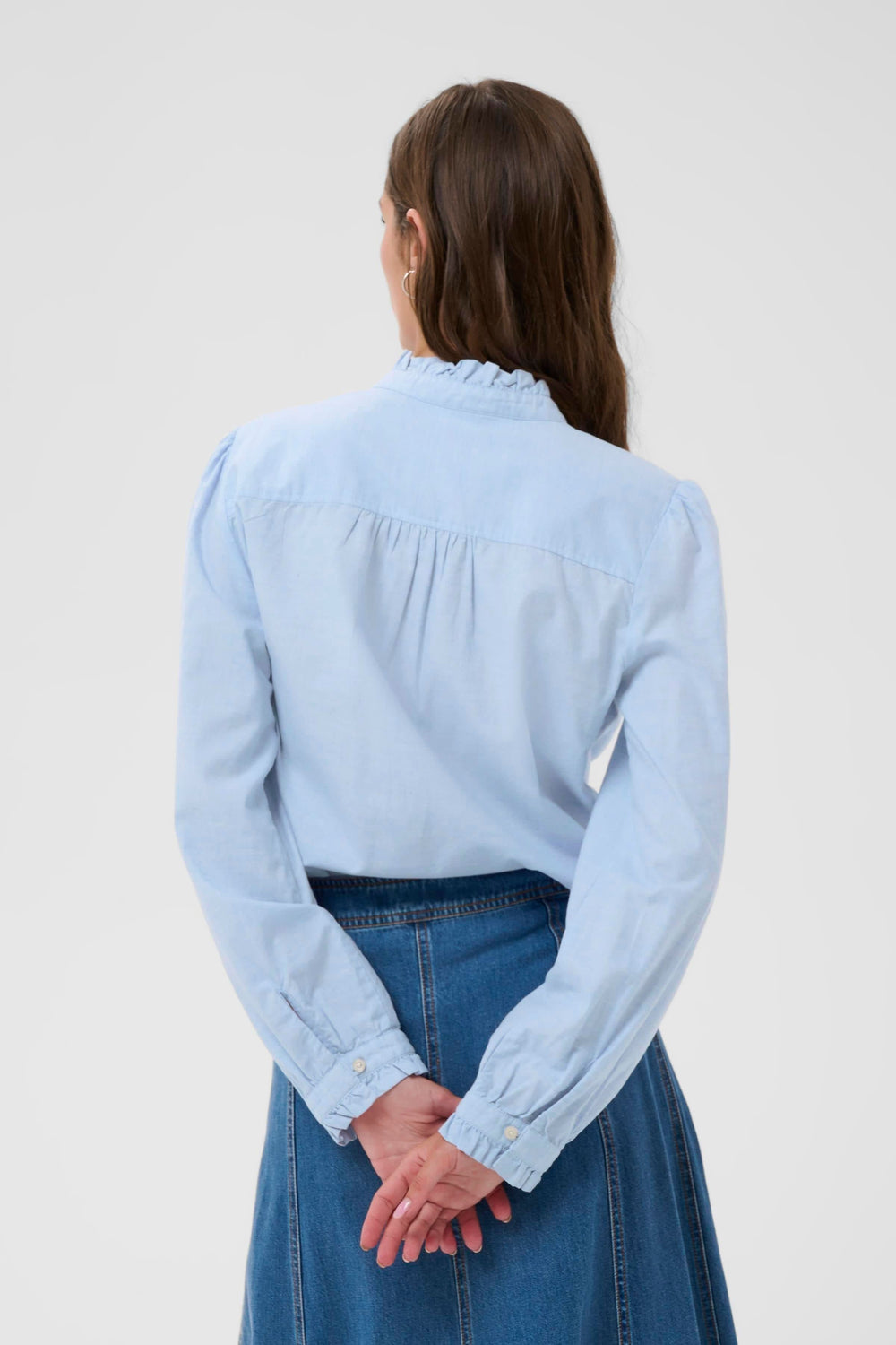 Dos d'une femme portant la Blouse Glessia bleue, jeans taille haute, col montant volanté.