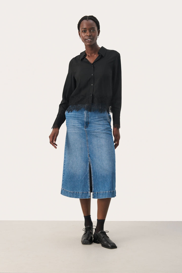 Femme portant une blouse noire élégante et une jupe en denim, parfaite pour un look moderne et élégant.