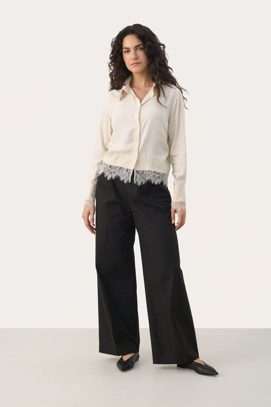 Blouse Lenina élégante avec dentelle, manches longues, portée avec un pantalon noir pour un look chic et confortable.