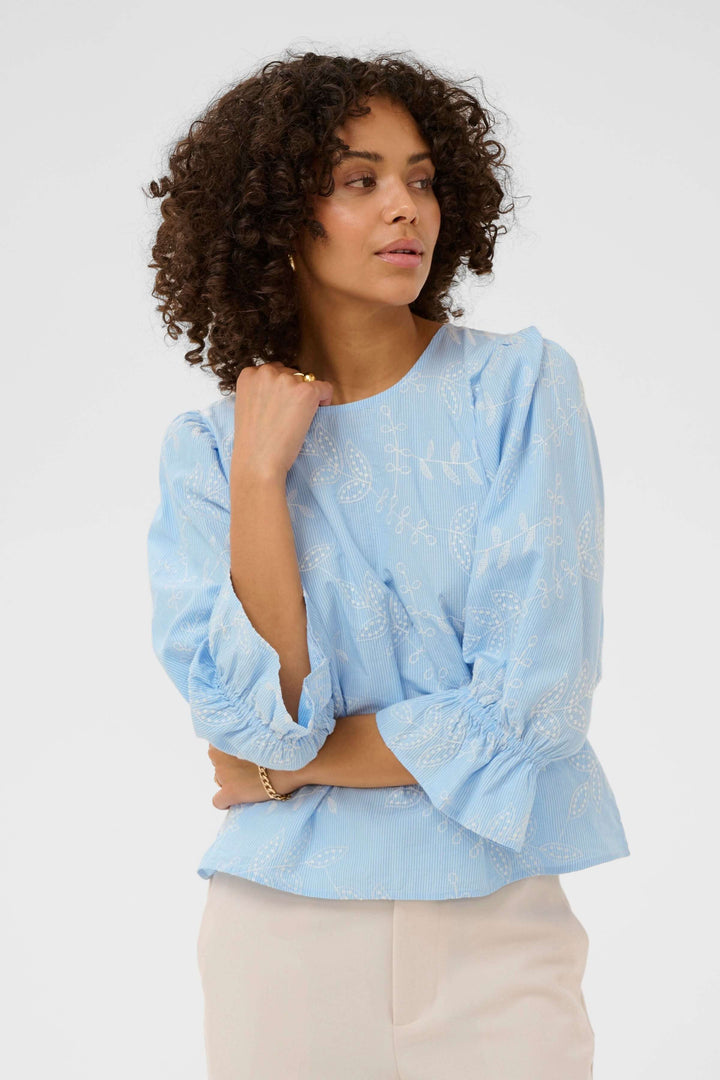 Blouse Marlee brodée à manches trois-quarts en bleu avec broderies délicates, manches froncées et coupe droite pour un style raffiné et décontracté.