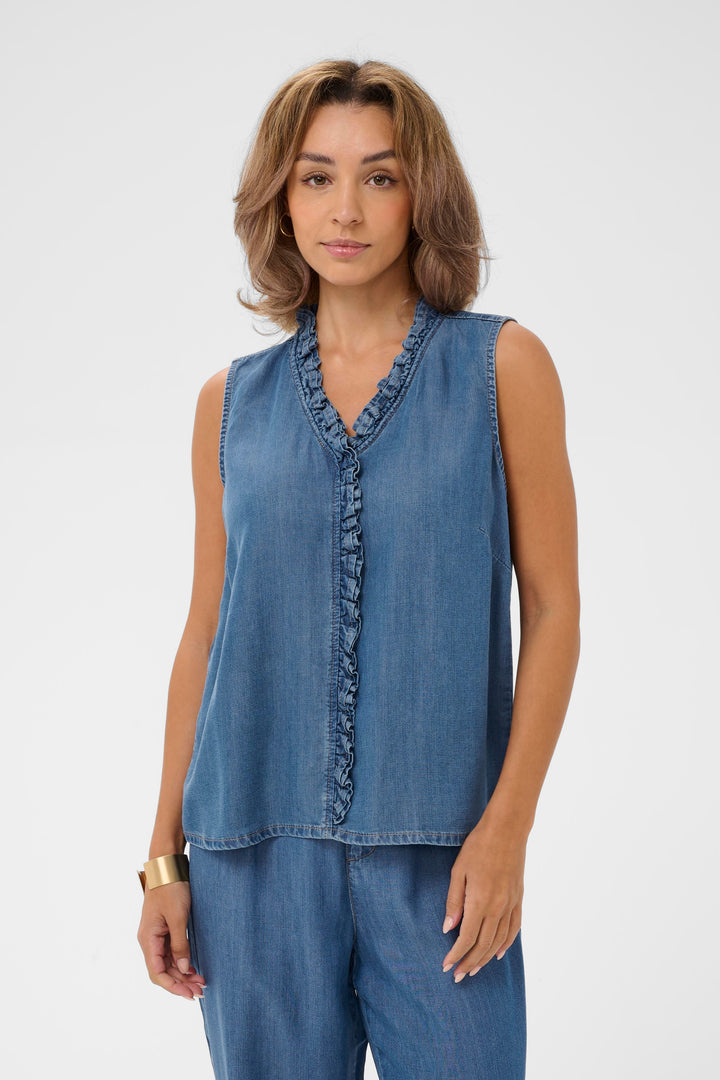 Blouse Molly sans manches en denim, avec encolure en V et détail volanté, portée par un modèle pour un look féminin et décontracté.