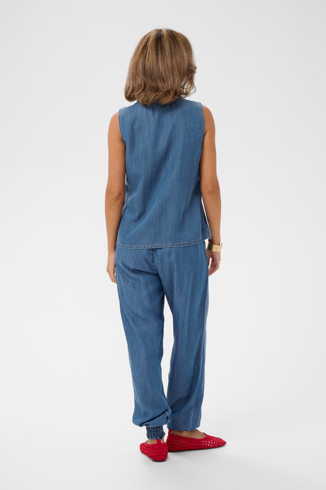 Femme portant la Blouse Molly sans manches en denim léger avec un pantalon assorti, vue arrière.