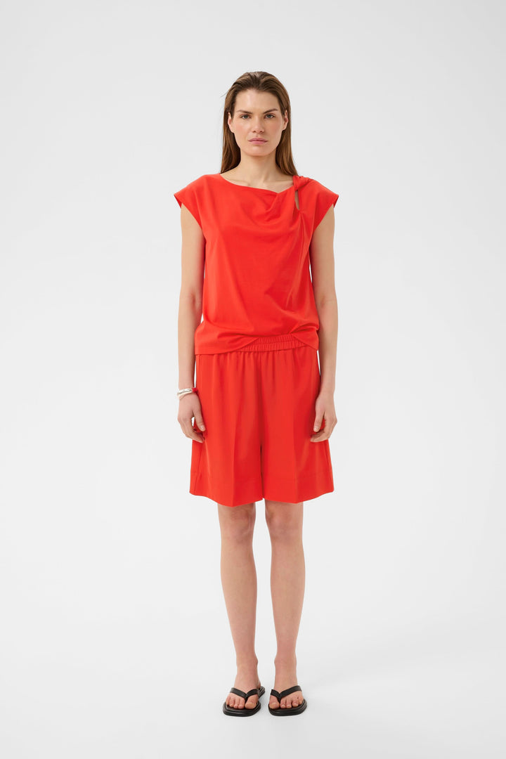 Blouse Pennie fluide à encolure drapée en rouge portée par un mannequin, offrant une touche élégante et moderne avec une coupe confortable.