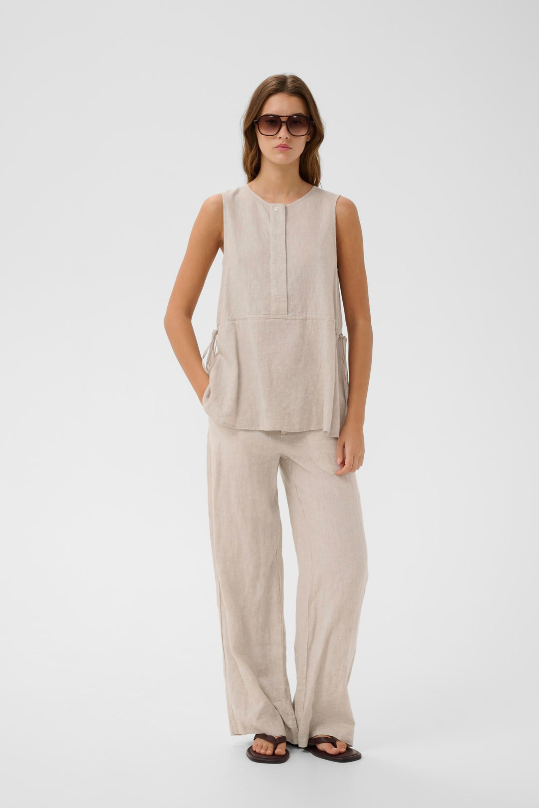 Femme portant la Blouse Rowan sans manches en lin, coupe fluide, avec un pantalon assorti, style minimaliste et moderne.