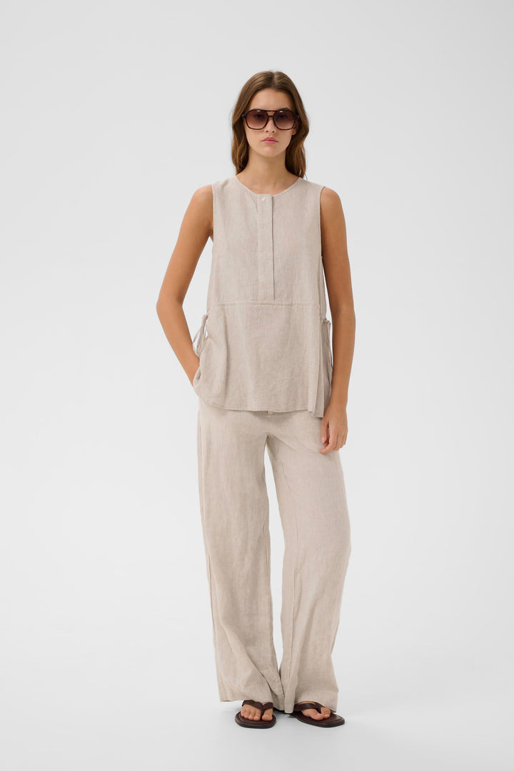 Femme portant la Blouse Rowan sans manches en lin, coupe fluide, avec un pantalon assorti, style minimaliste et moderne.