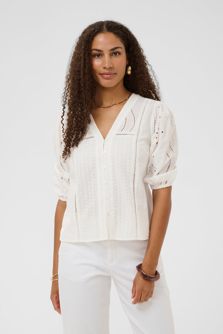 Femme portant la Blouse Signe avec des détails ajourés et broderies raffinées, encolure en V, coupe fluide, élégance assurée.