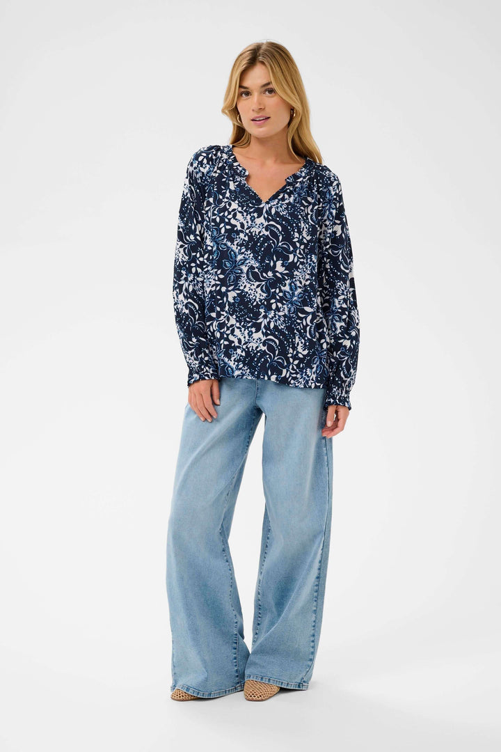 Femme portant la Blouse Tiah fluide à imprimé floral avec encolure en V et manches longues, tenue élégante et moderne en bleu.