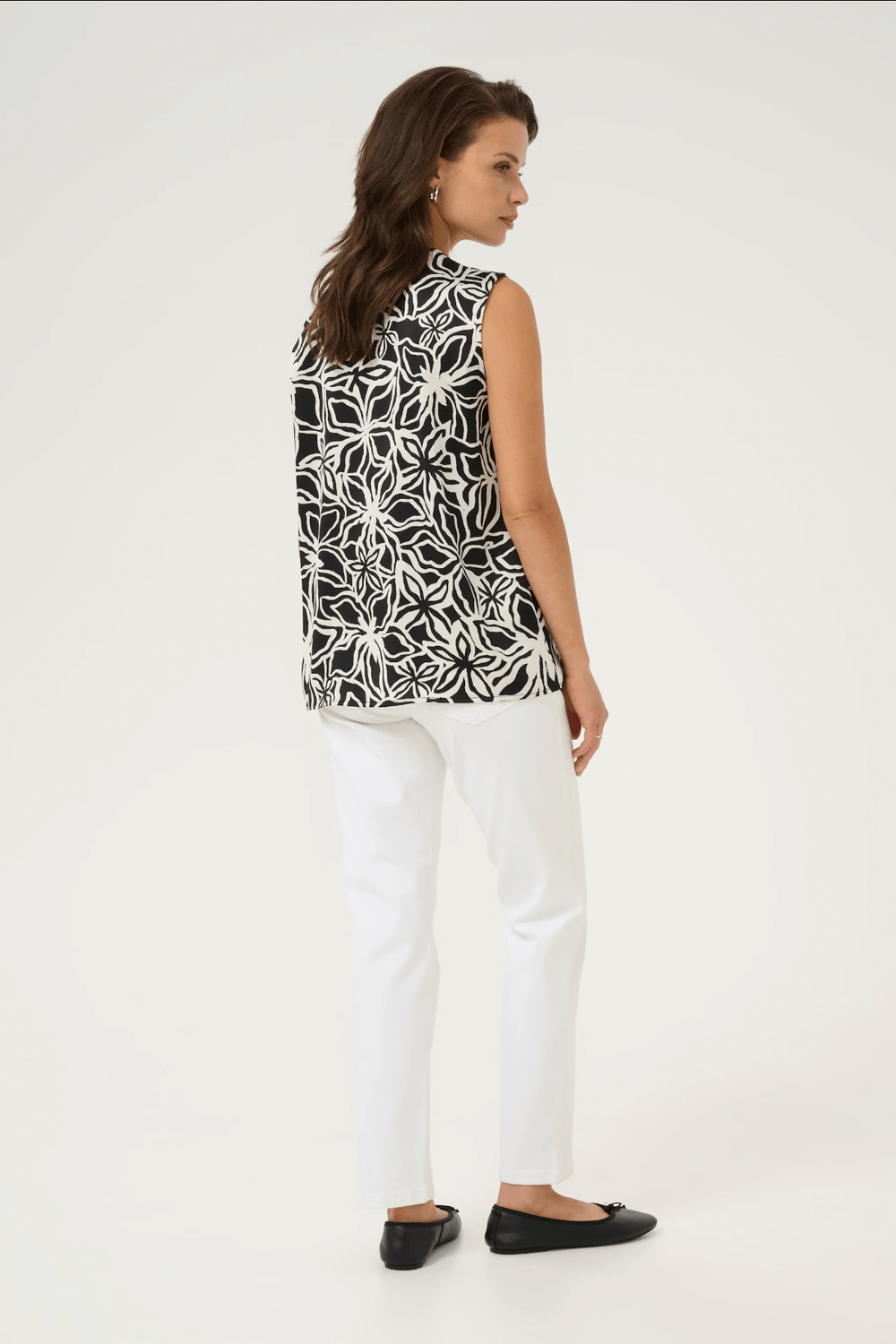 Femme portant une blouse à motif noir et blanc, vue de dos, associée à un pantalon blanc.