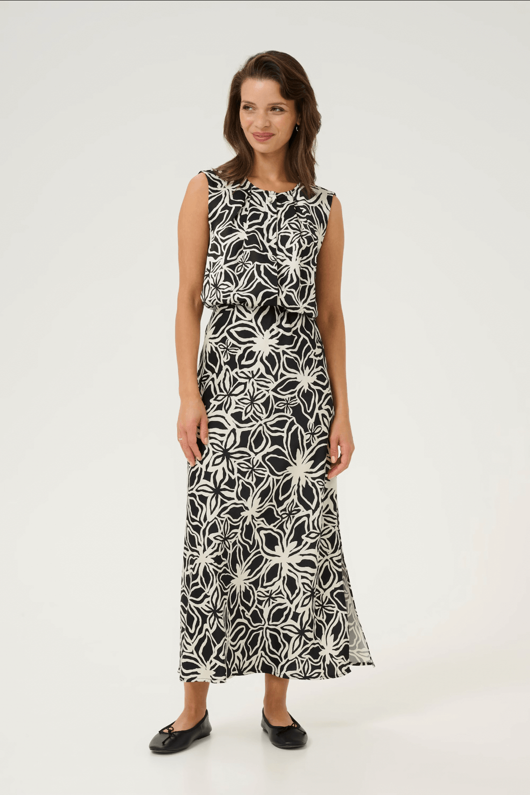 Femme souriante portant une blouse à imprimé fleuri noire et blanche, idéale pour un look chic et féminin.