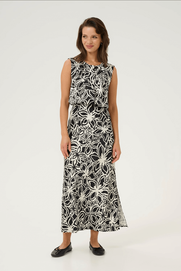 Femme souriante portant une blouse à imprimé fleuri noire et blanche, idéale pour un look chic et féminin.
