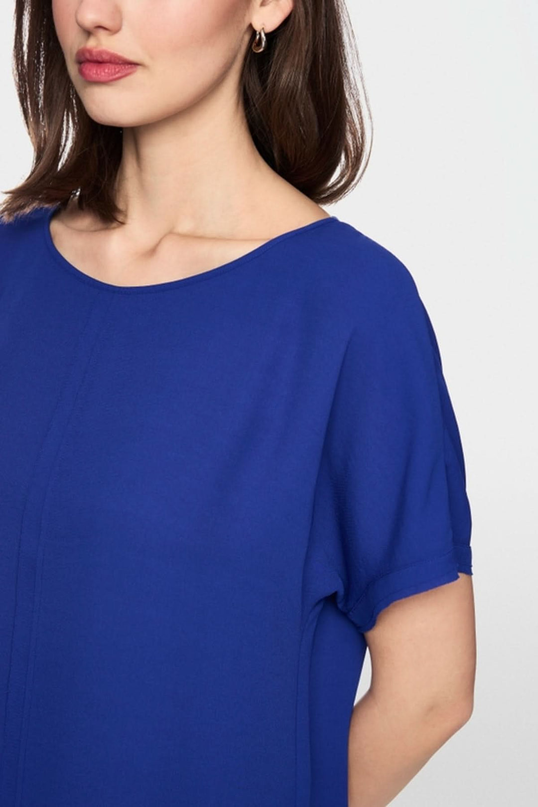 Femme portant une blouse ample en tissu fluide bleu avec col rond et manches courtes, parfaite pour les journées chaudes.