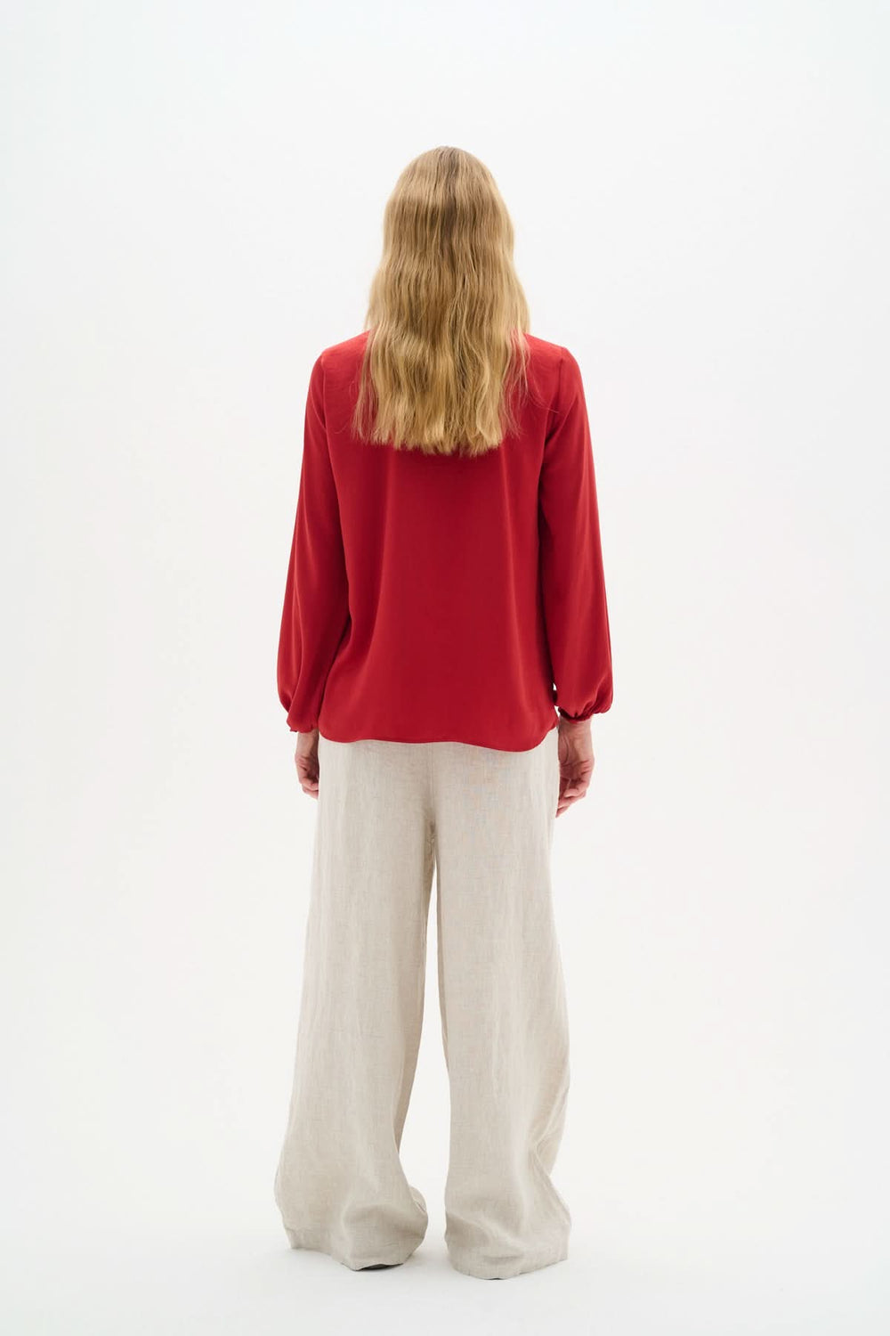 Femme vue de dos portant une blouse rouge col en V avec manches longues et pantalon beige ample.