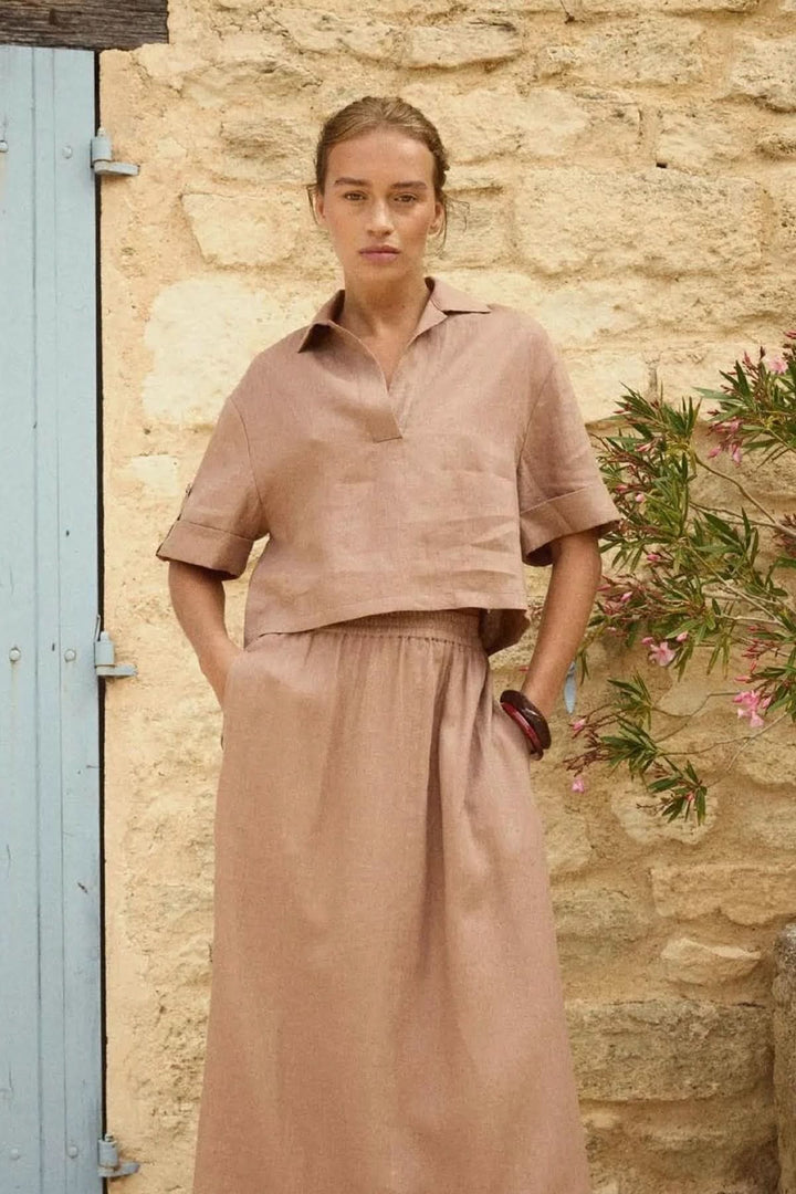 Femme portant une blouse courte en lin à col ouvert, élégante et décontractée, contre un mur en pierre, idéale pour l&