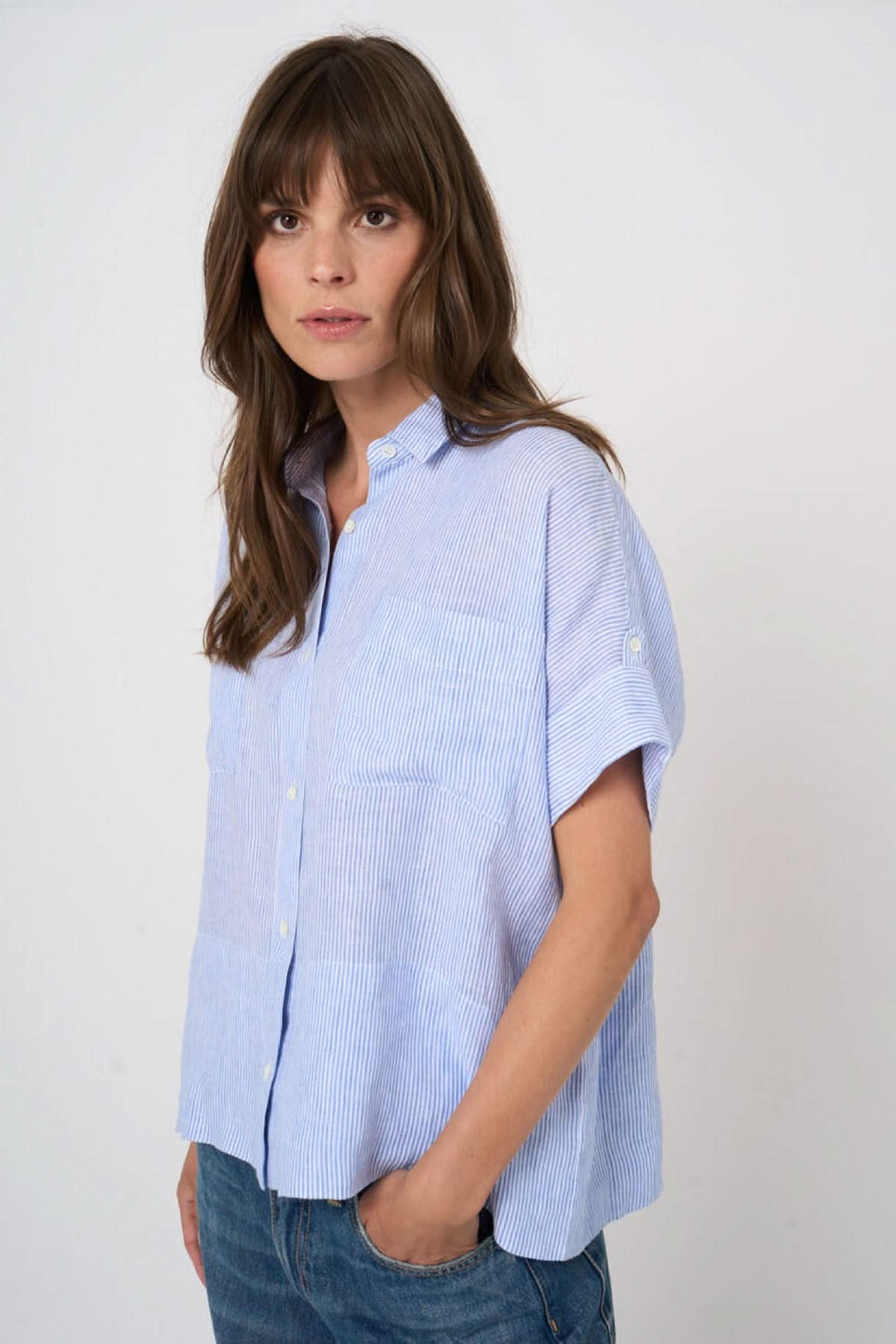 Femme portant une blouse en lin à rayures fines, manches courtes, fermeture boutonnée, col classique, coupe droite, style décontracté.