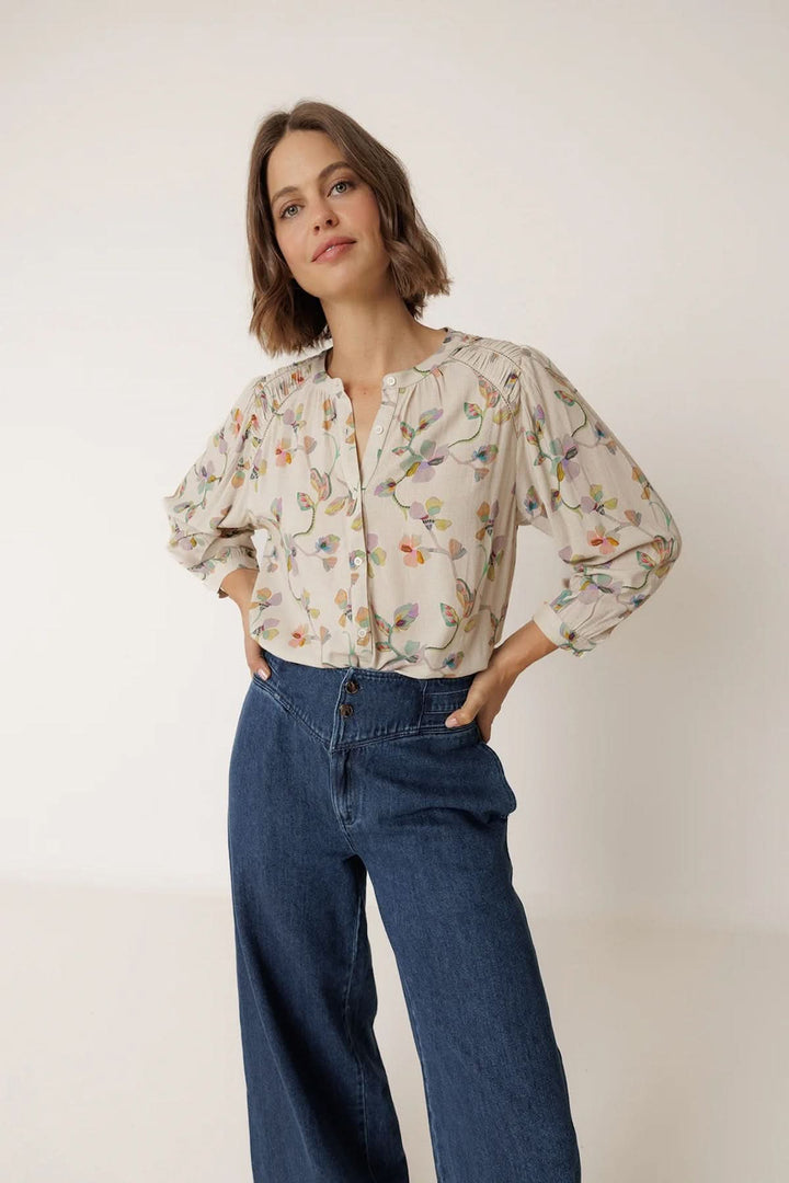 Blouse florale à manches longues avec imprimé délicat et encolure ouverte, portée avec un jean pour une tenue élégante et féminine.