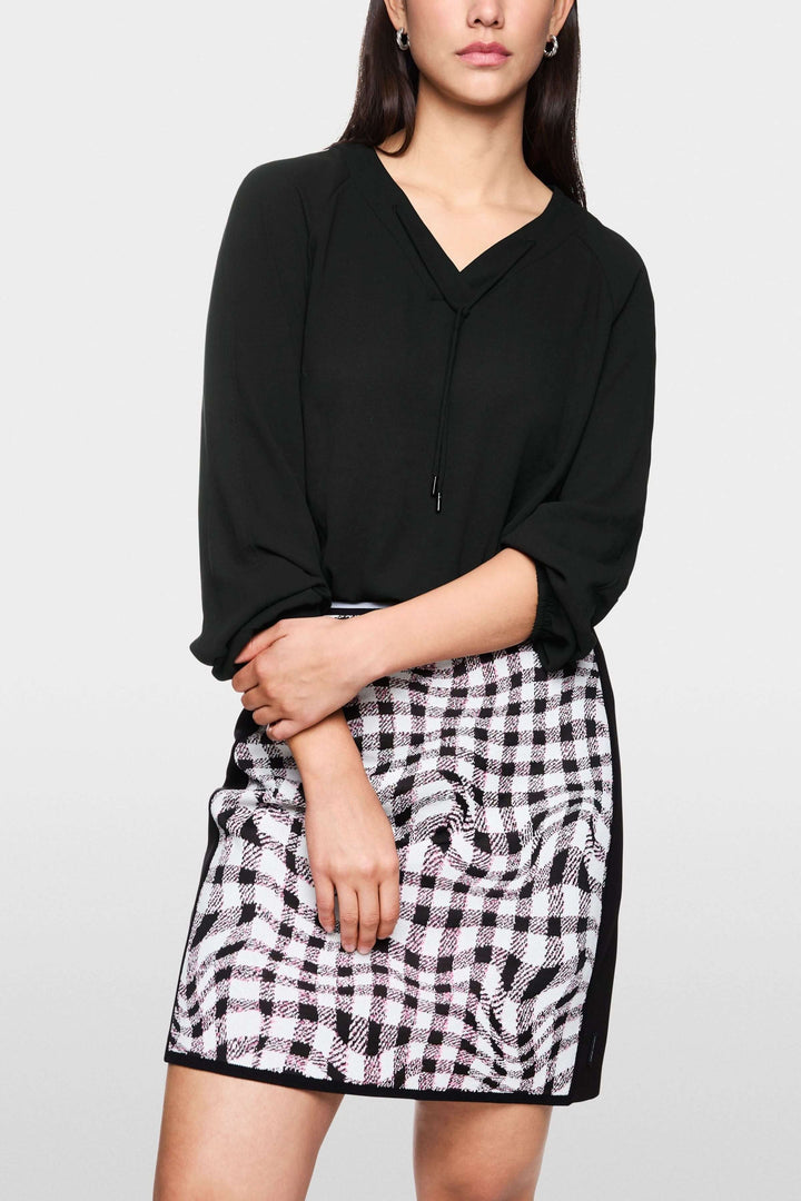 Femme portant une blouse fluide noire à encolure en V avec manches légèrement bouffantes, associée à une jupe imprimée chic.
