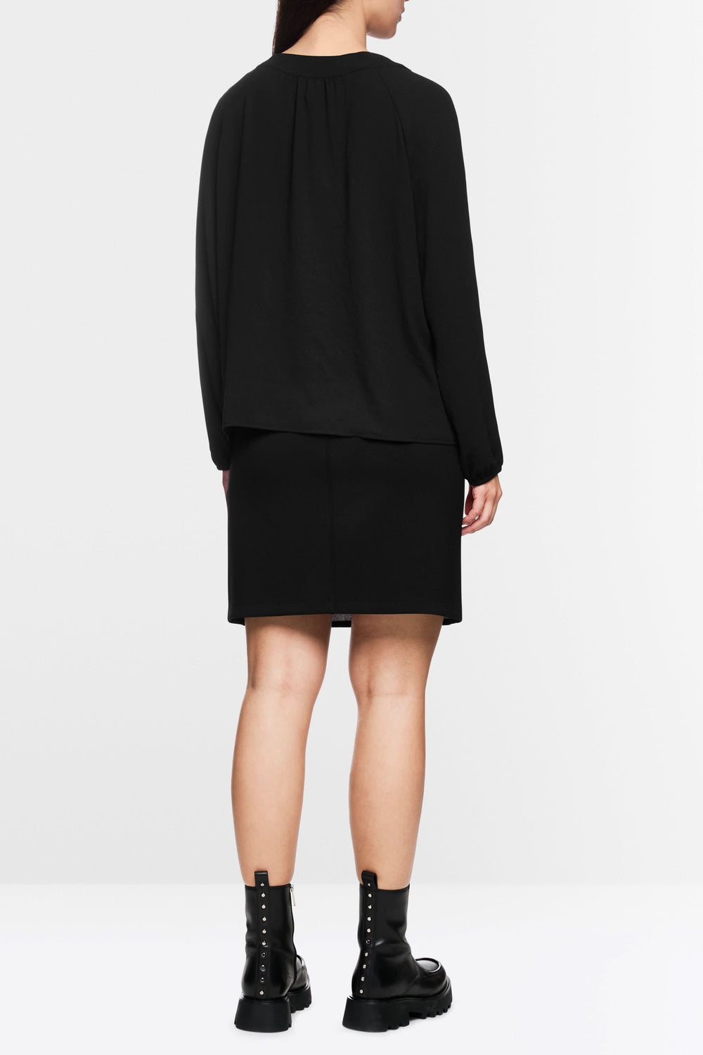 Vue arrière de la blouse fluide noire, manches longues bouffantes, portée avec une jupe noire et des bottines.