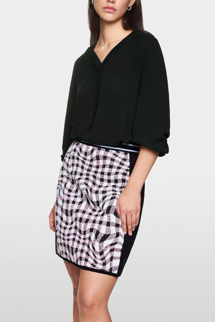 Blouse fluide noire avec encolure en V et manches longues bouffantes, portée avec une jupe imprimée.
