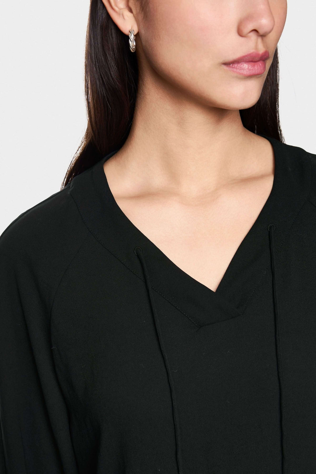 Blouse fluide noire à encolure en V et manches longues, style minimaliste et moderne pour le bureau ou les sorties, sur mannequin.