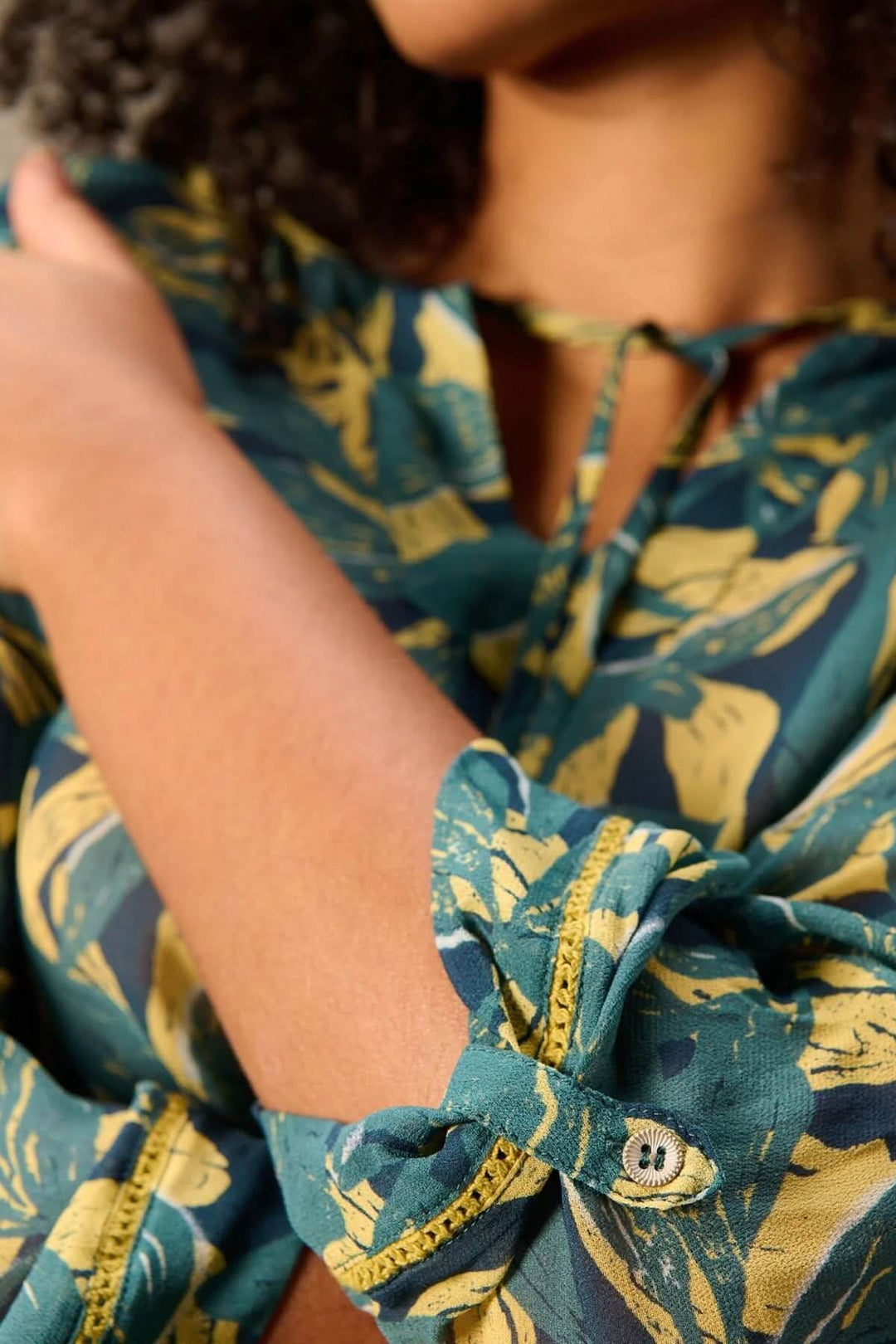 Blouse fluide imprimé avec manches 3/4 et encolure nouée, détail du tissu végétal audacieux en gros plan.
