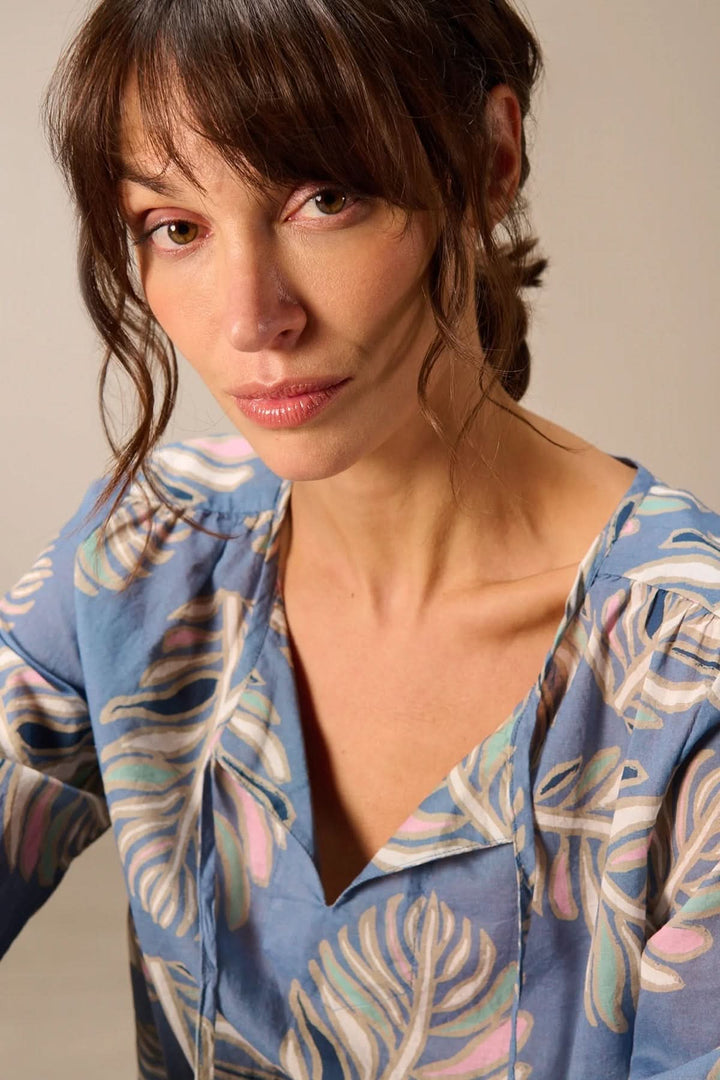 Femme portant une blouse fluide à manches longues avec motif floral, idéale pour le bureau ou les sorties, ajoutant élégance et confort.