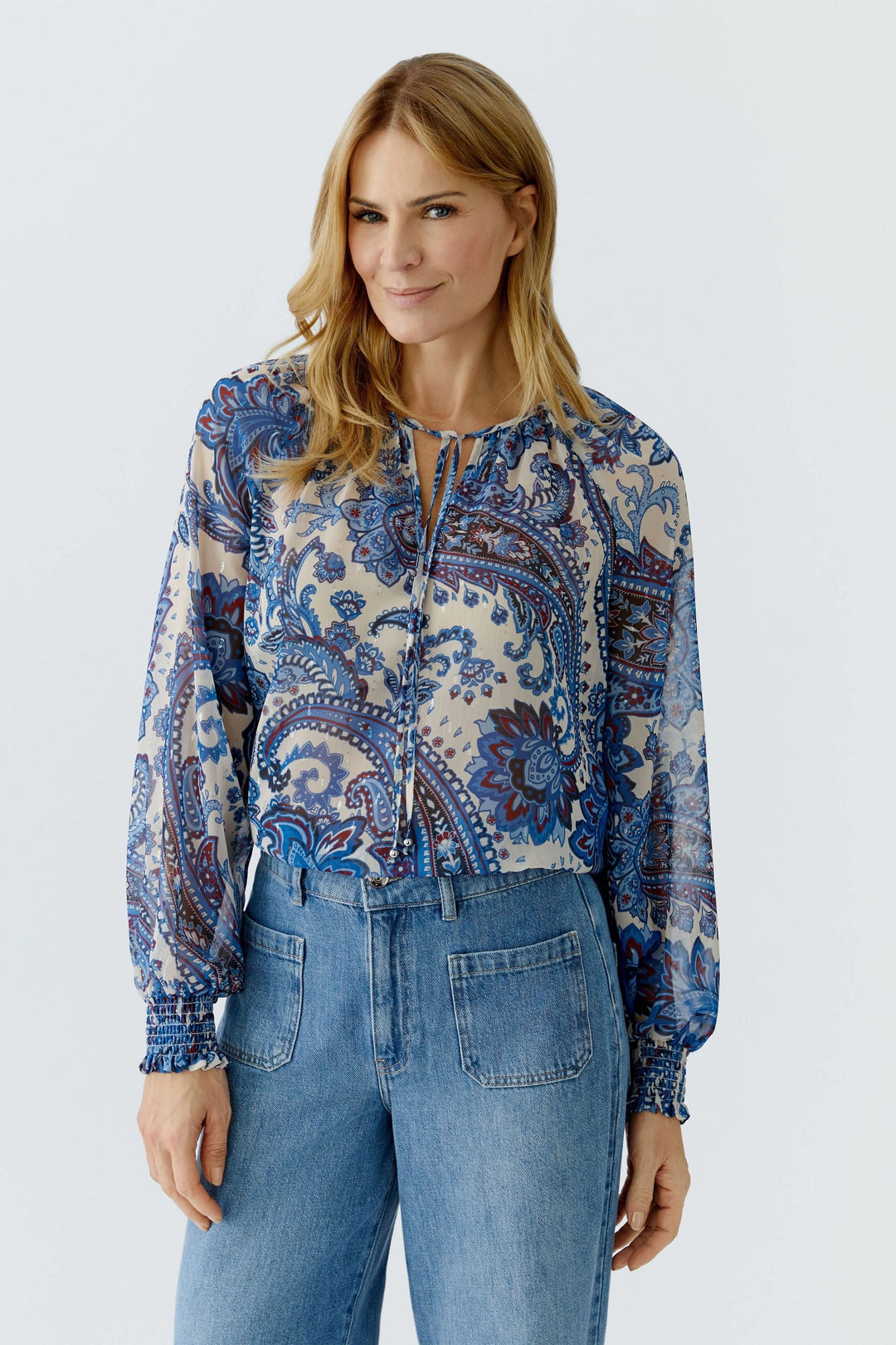 Femme portant une blouse imprimée à manches longues avec motif cachemire bohème, encolure nouée, sur un jean.
