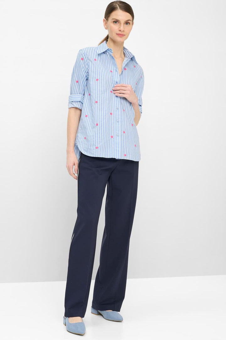 Femme portant une blouse rayée à broderies contrastantes VIKI avec pantalon bleu, style moderne et fluide.