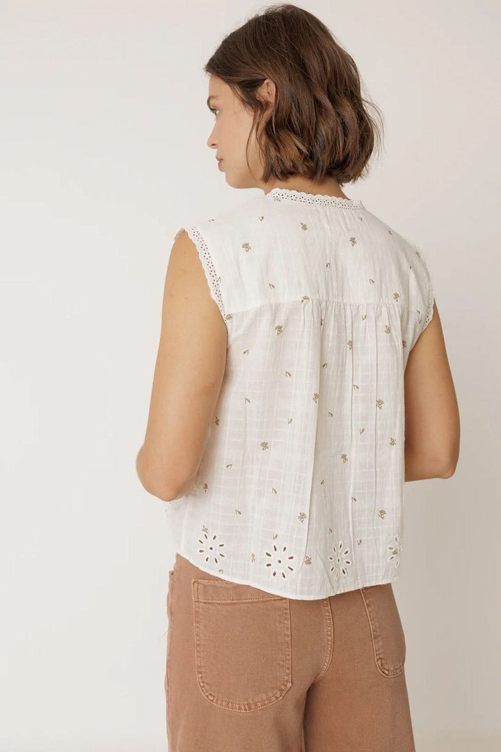 Femme portant une blouse sans manches à détails ajourés avec bordure festonnée et motifs élégants.