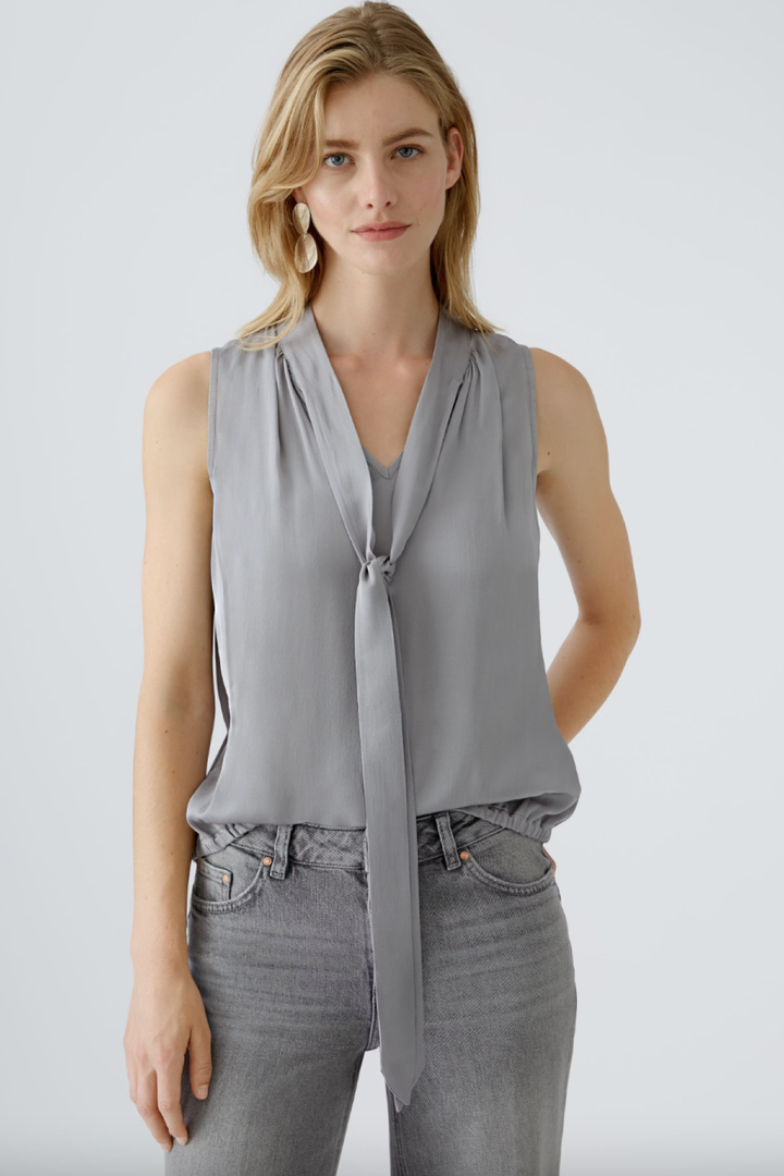 Blouse en satin gris avec cravate, coupe décontractée et encolure en V, portée avec un jean.