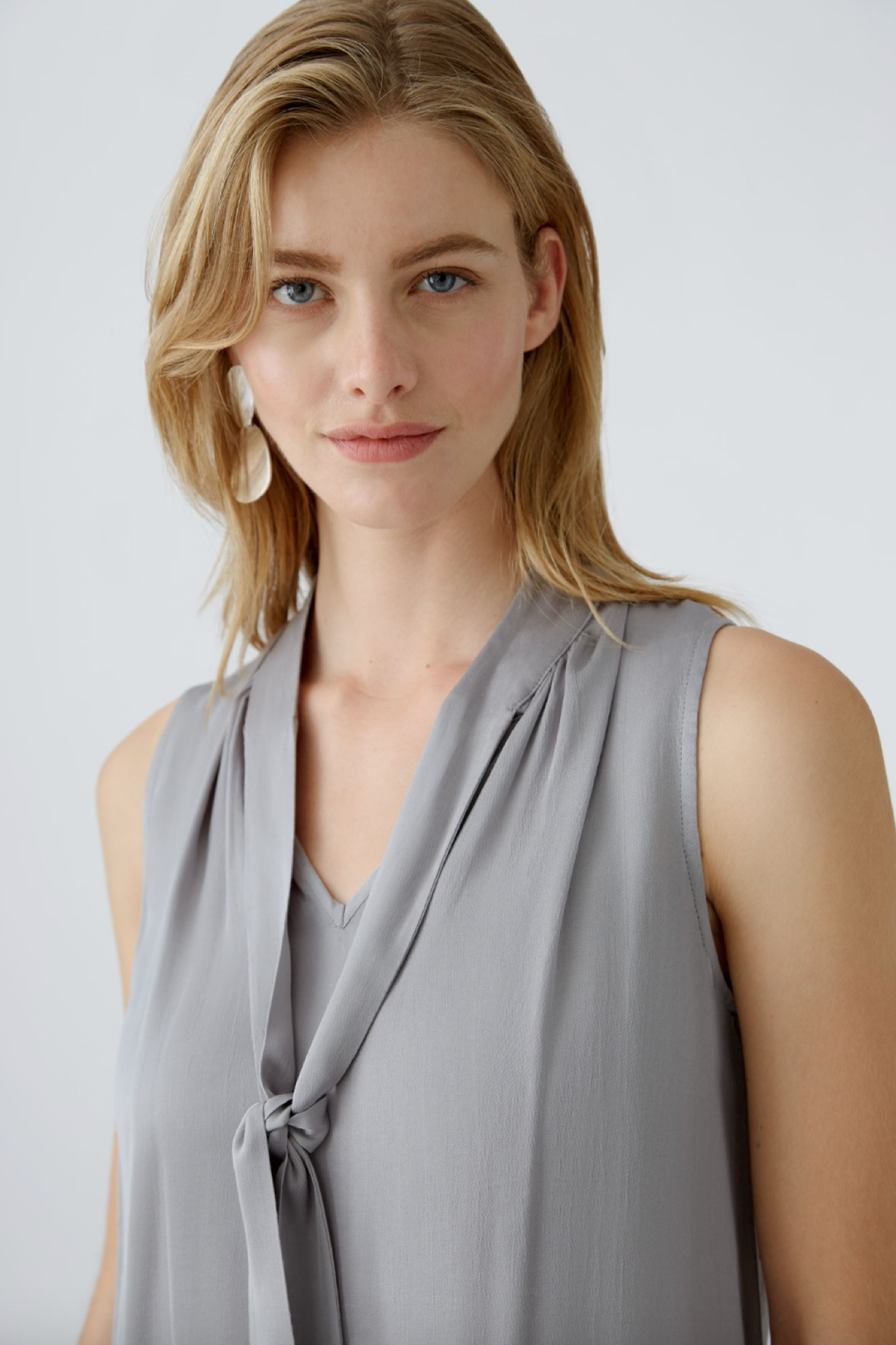 Blouse en satin brillant avec cravate, encolure en V et coupe décontractée, portée par modèle blonde.