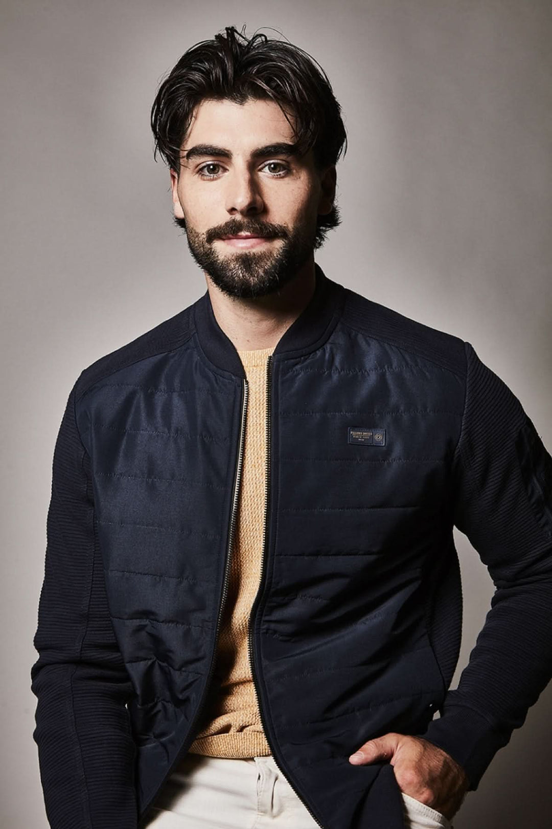 Homme portant un blouson matelassé à fermeture zippée, col montant, couleur sombre, style moderne et élégant.