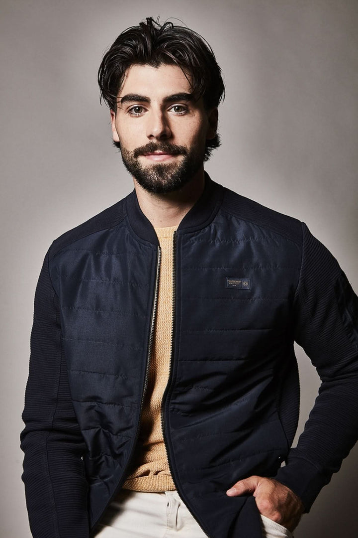 Homme portant un blouson matelassé à fermeture zippée, col montant, couleur sombre, style moderne et élégant.