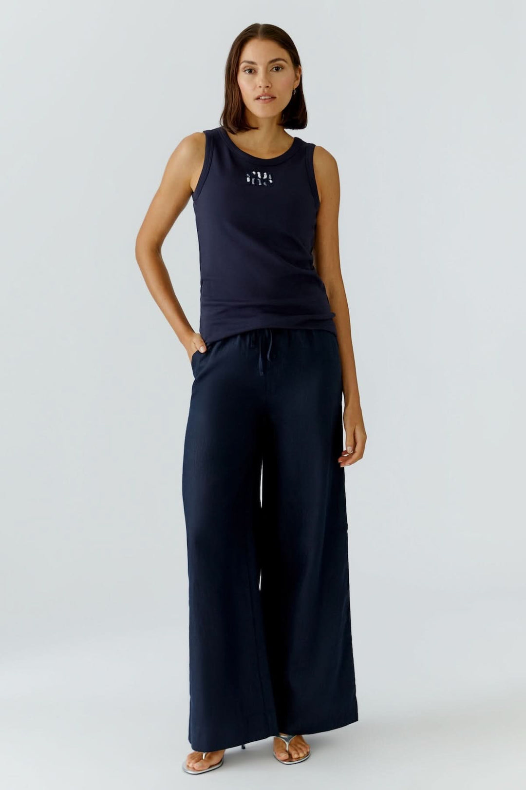 Femme portant une camisole ajustée avec détail graphique, coupe féminine épurée, encolure ronde, sans manches, idéale pour superposer.