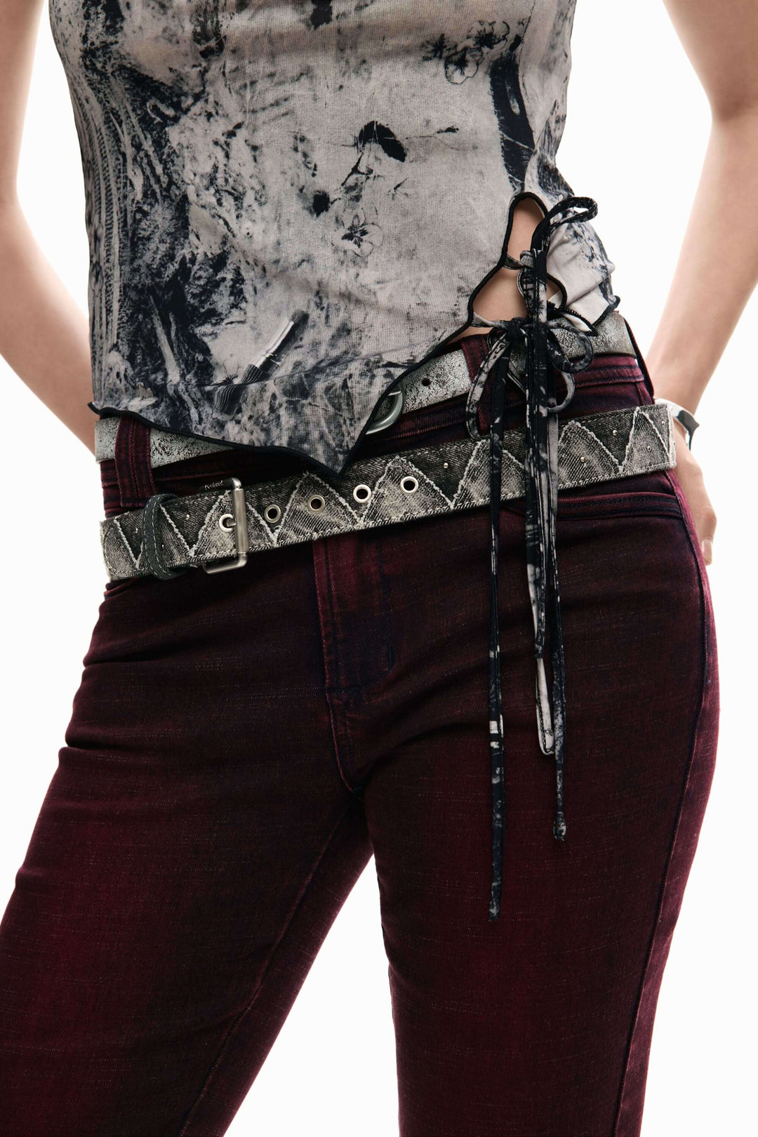 Camisole ajustée à imprimé artistique avec détail de laçage, tenue moderne et audacieuse, portée avec un pantalon rouge foncé.