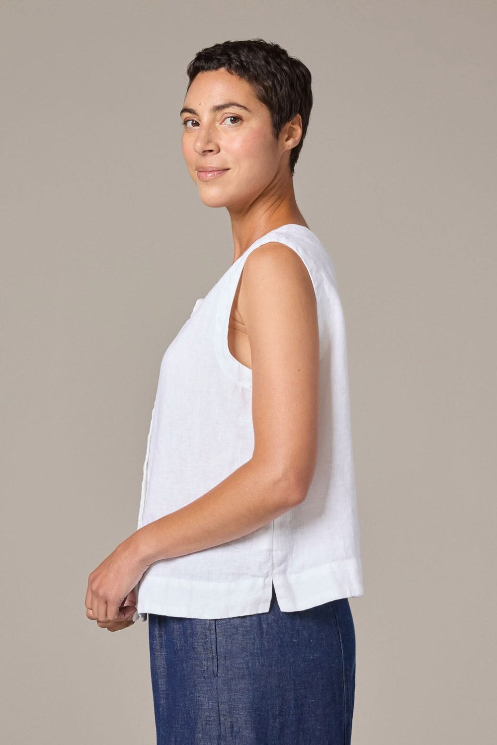 Femme portant une camisole boutonnée en lin blanche, coupe droite, style décontracté et raffiné.