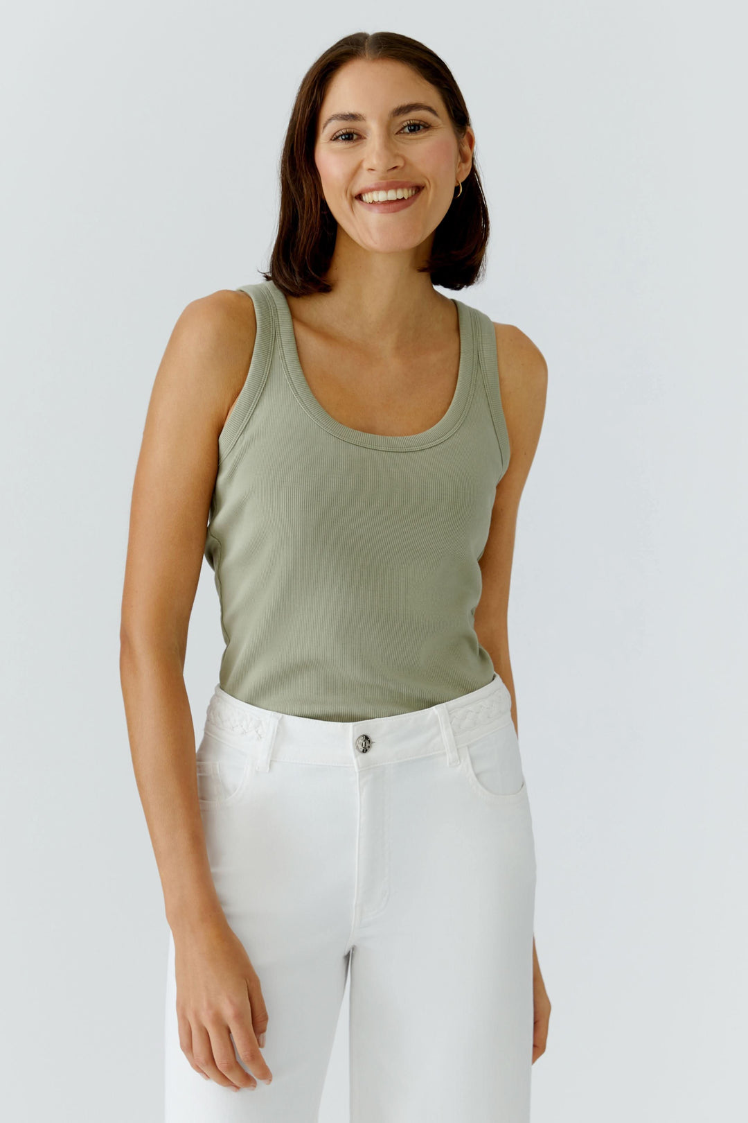 Femme portant une camisole côtelée essentielle verte, coupe ajustée, idéale pour superpositions ou tenue seule, confortable et polyvalente.