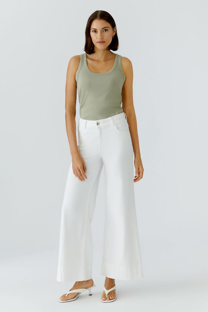 Femme portant une camisole côtelée essentielle verte avec un pantalon large blanc, look décontracté et élégant.
