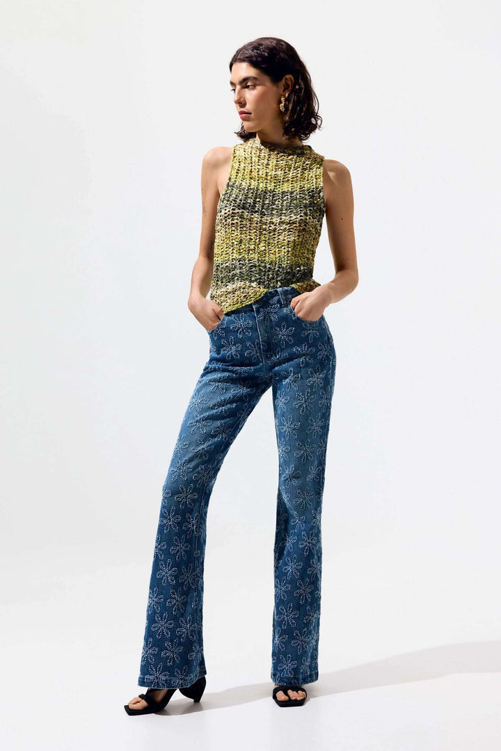 Femme portant une camisole en tricot texturé sans manches jaune avec un jean imprimé floral.