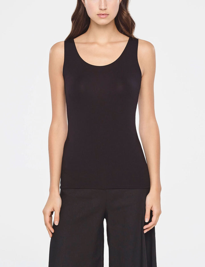 Femme portant une camisole essentielle ajustée sans manches en noir, coupe minimaliste et polyvalente, matière douce et extensible.